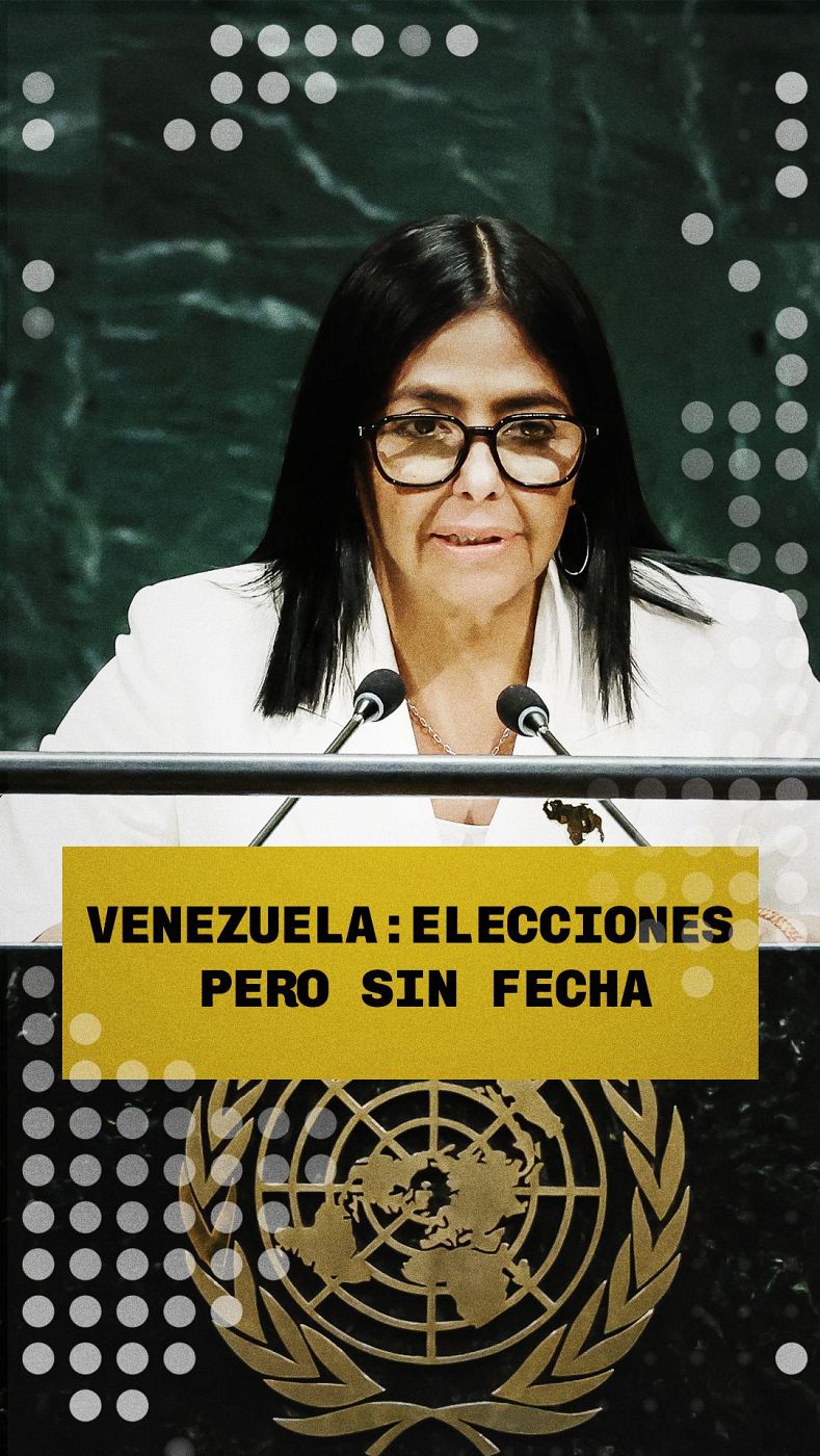 Delcy Rodríguez, Vicepresidenta Ejecutiva de Venezuela, habla en un evento de la ONU. Lleva blazer blanco y gafas. Banner amarillo: "VENEZUELA: ELECCIONES PERO SIN FECHA".