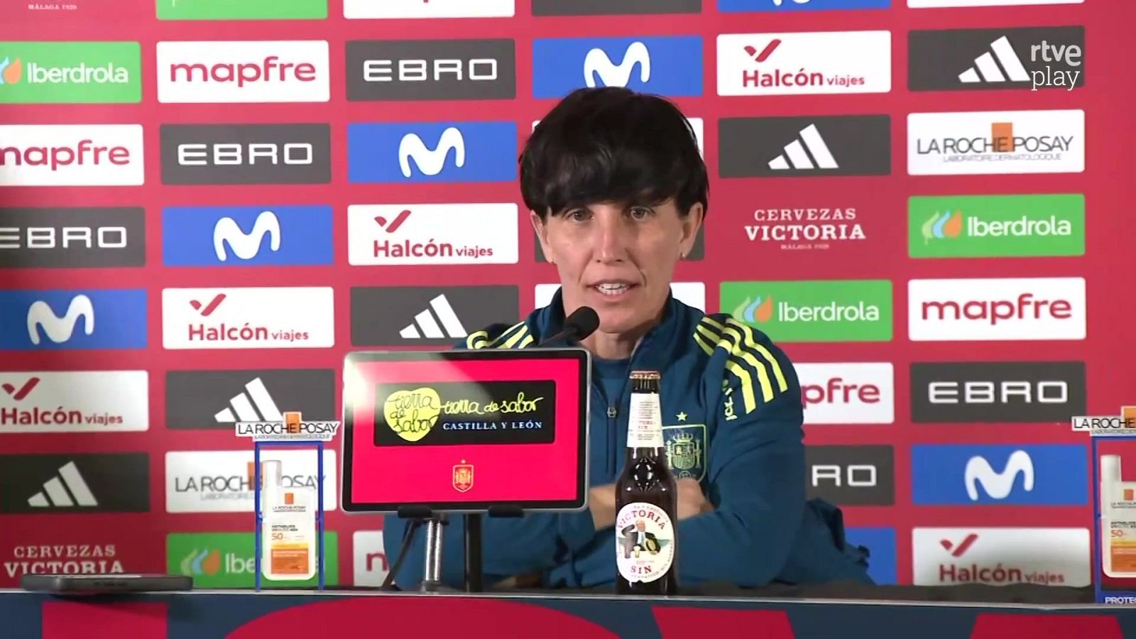 La seleccionadora Montse Tomé comparece en rueda de prensa con la sudadera azul de la RFEF ante un panel corporativo con patrocinadores.