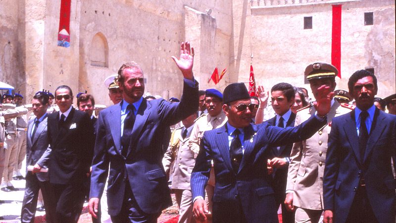 Fotografía histórica de los reyes Juan Carlos I y Hasán II caminando juntos en un patio palaciego durante una visita oficial en 1979, rodeados por su comitiva.