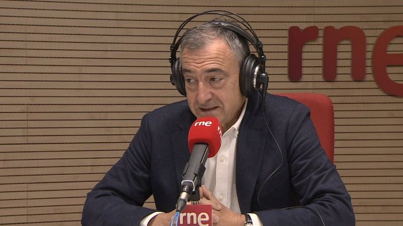 Hombre de mediana edad con americana azul y auriculares en un estudio de radio, hablando ante un micrófono con el logotipo de la emisora.
