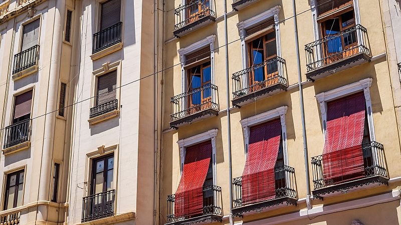 Fachadas soleadas de edificios residenciales tradicionales con balcones de hierro y persianas de madera en una jornada calurosa.