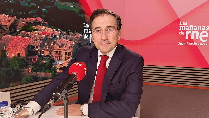 José Manuel Albares sonríe durante una entrevista en un estudio de radio, sentado ante una mesa con un micrófono de Radio Nacional de España.