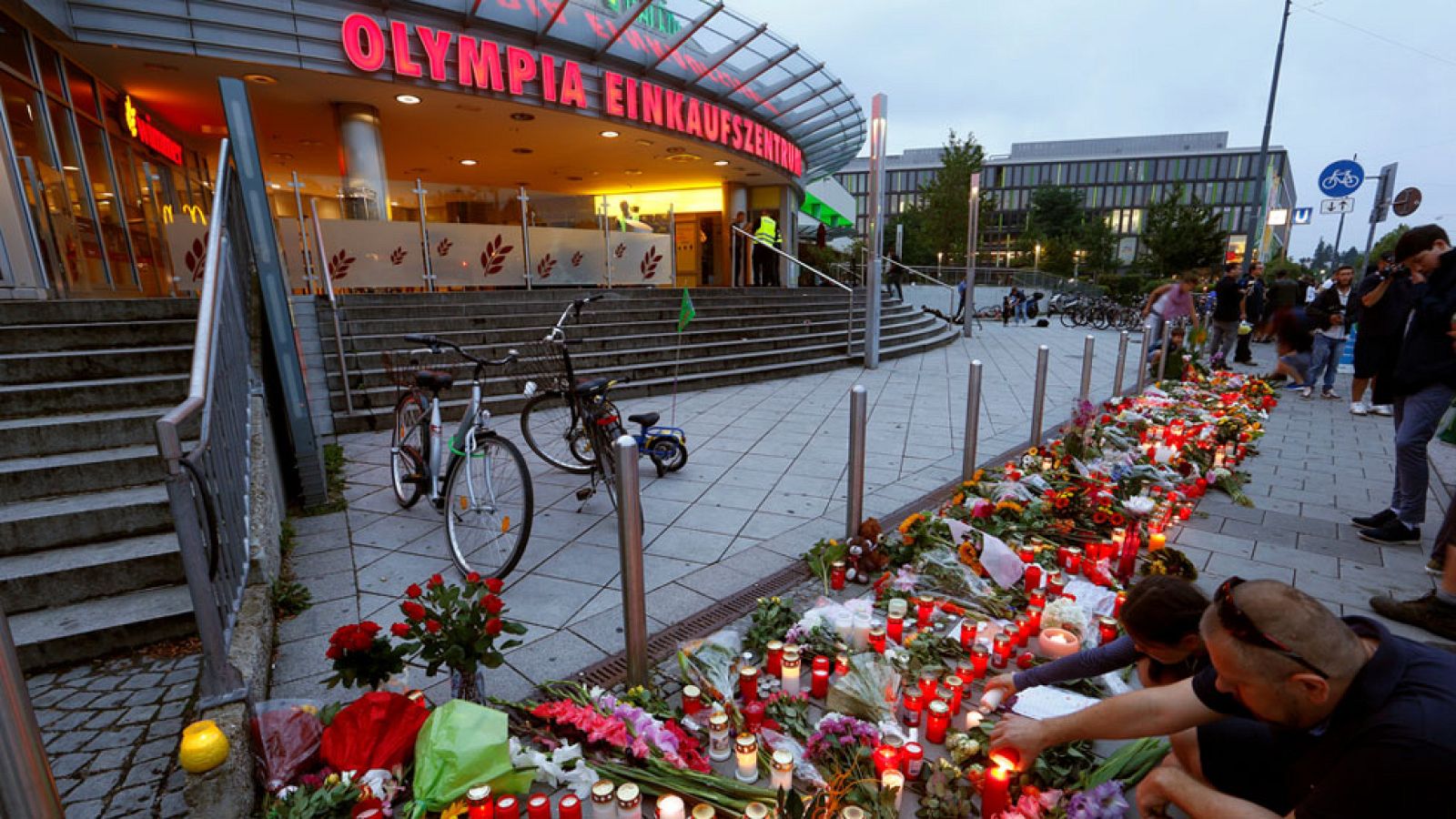 Los habitantes de Múnich se han acercado al centro comercial Olympia, el lugar en el que este viernes se produjo un tiroteo que acabó con la vida de nueve personas. El autor, que todo apunta que actuó bajo la locura, se suicidó poco después.Frente al centro comercial, los muniquenses han depositado flores y velas en recuerdo a las víctimas de esta nueva masacre.