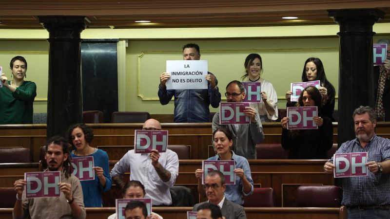 Decenas de diputados de Unidos Podemos han protagonizado una protesta al inicio del pleno del Congreso exhibiendo carteles con las iniciales DH, de Derechos Humanos, que han depositado después en el escaño del ministro del Interior, Jorge Fernández D