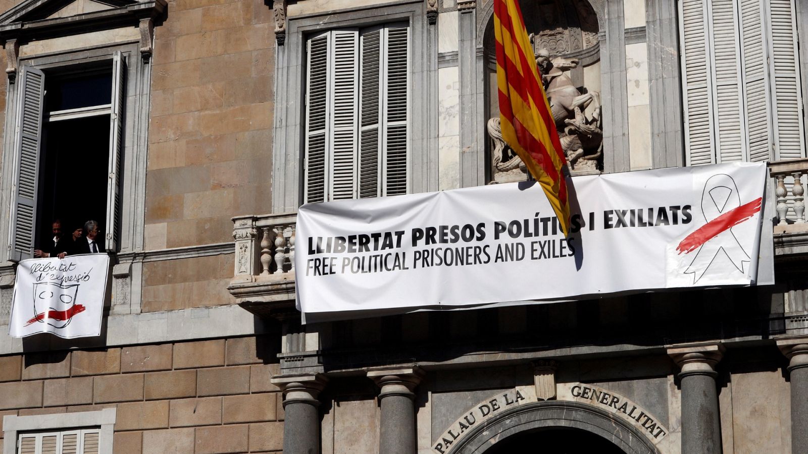 En la mañana de este jueves, varias personas han salido al balcón de la fachada principal del Palau de la Generalitat y han tapado la pancarta con el lazo amarillo con otra que también pide "libertad para los presos políticos y exiliados", pero con u