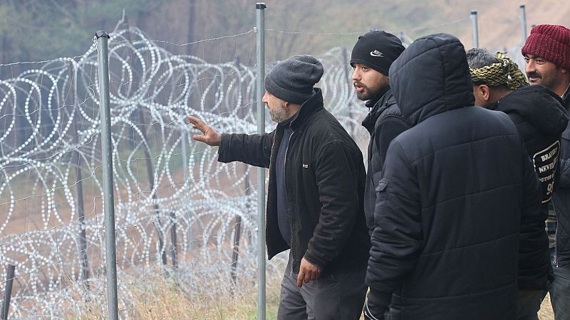 Un grupo de migrantes reunidos en torno a la valla fronteriza
