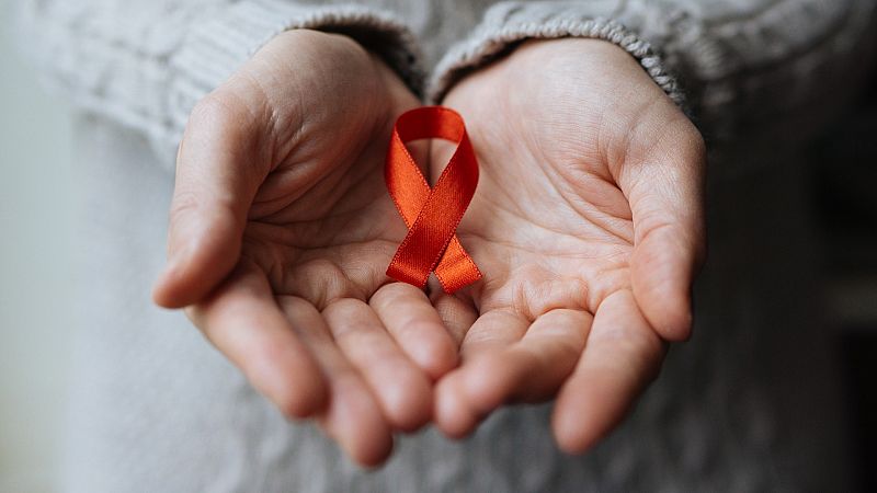 Una persona sostiene un lazo rojo entre sus manos, símbolo de la lucha contra el VIH