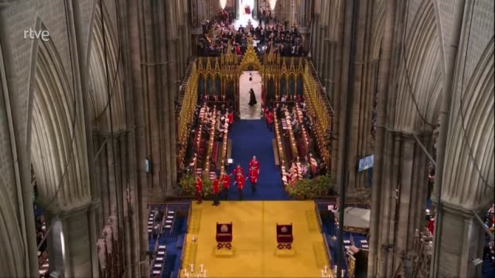 Fragmento de la emisión de la BBC de la coronación de Carlos III y Camila en la Abadía de Westminster donde se ve a un sacristán vestido con una túnica negra y un bastón.